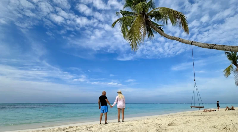 Couple walking on a white-sand beach on a Maldives local island — turquoise water and tropical scenery.