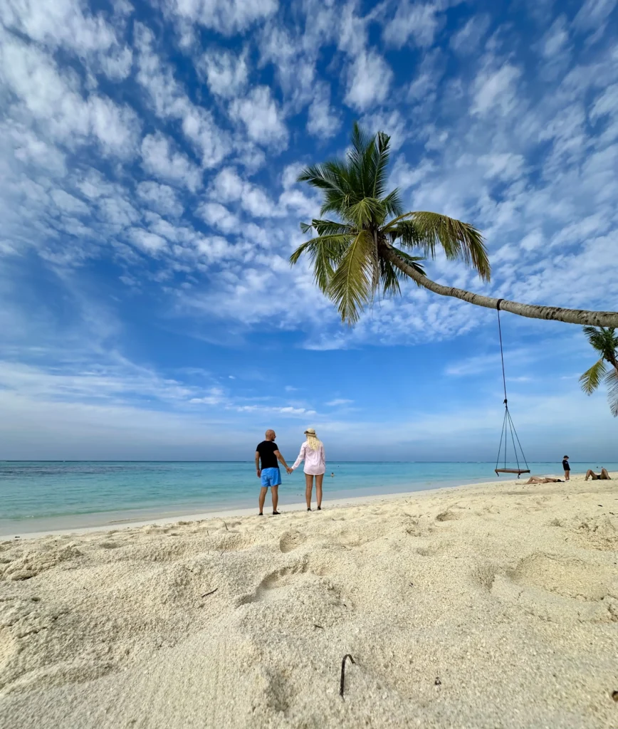 Couple walking on a white-sand beach on a Maldives local island — turquoise water and tropical scenery.